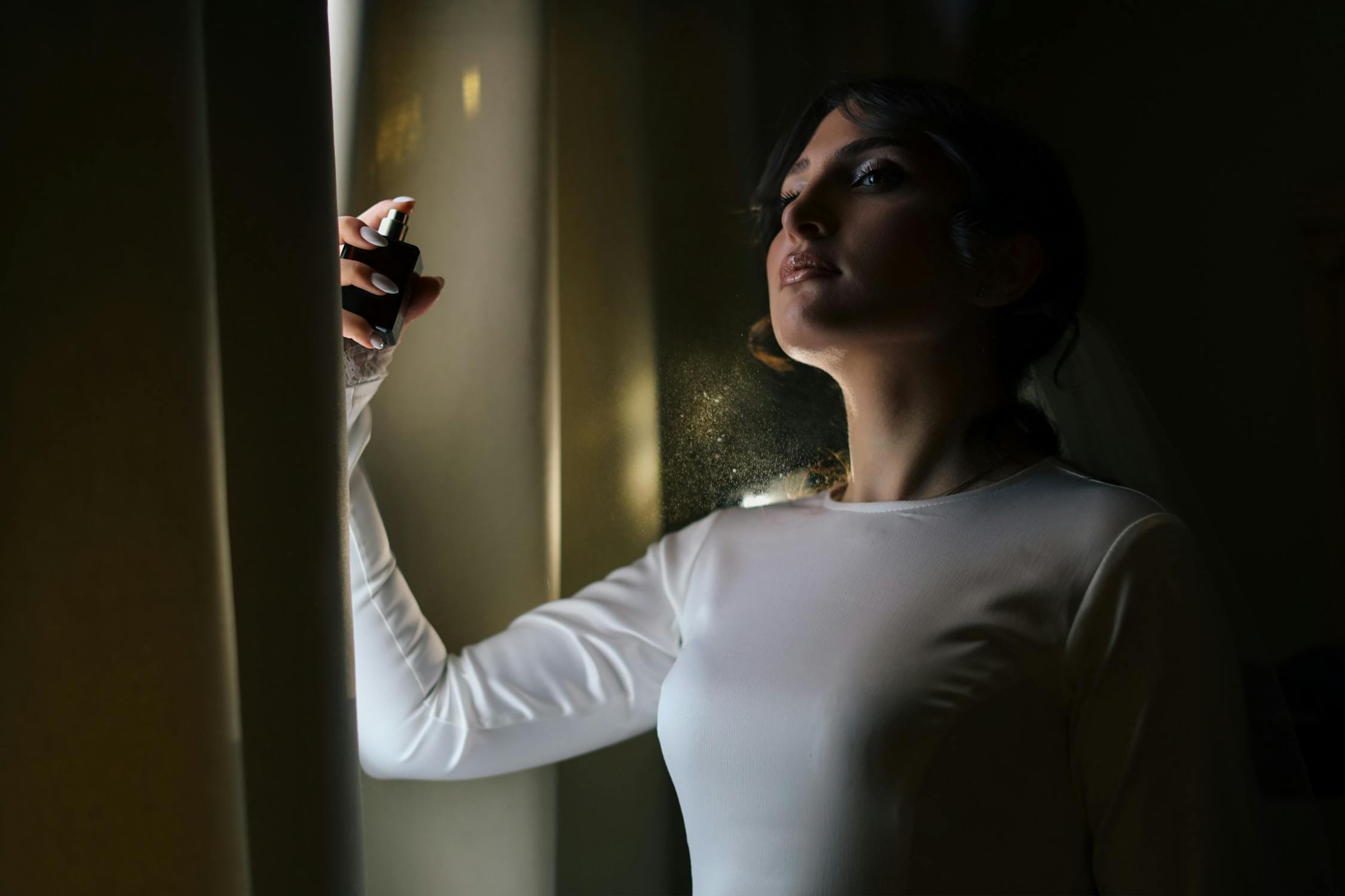 free photo of bride applying perfume in dramatic lighting