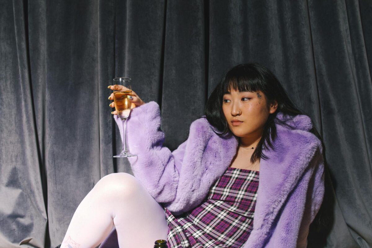 Fashionable Asian woman in purple coat with a wine glass at a party setting.